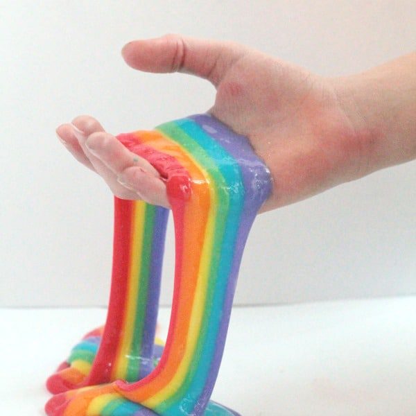 Kid hands holding red, orange, yellow, green, blue, and purple rainbow slime.