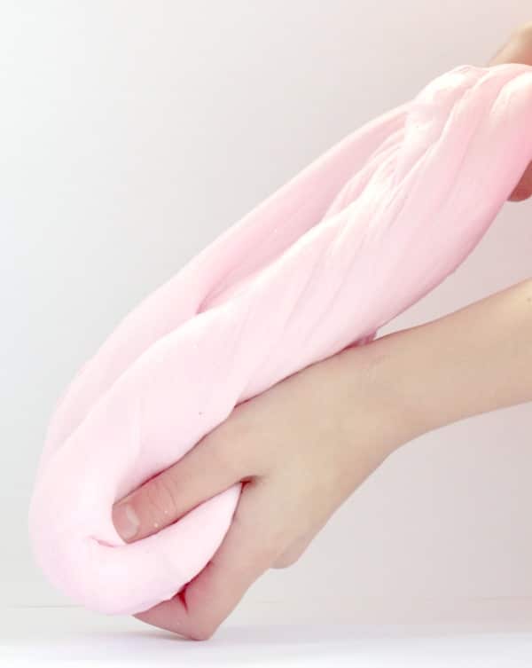 Hands stretching pink fluffy slime showing how to make fluffy slime with shaving cream.