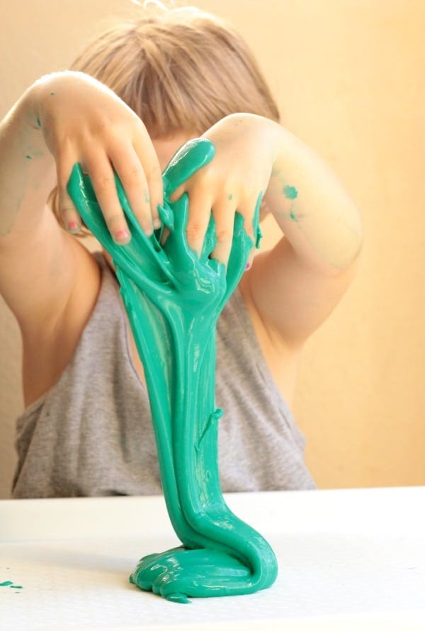 Kid hands playing with and stretching a green liquid slime recipe.