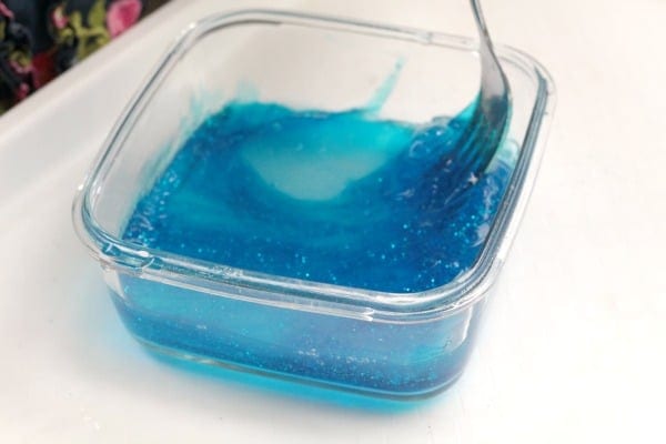 Blue glitter slime in a clear container stirred with a fork. Shows ocean slime with broax in process.
