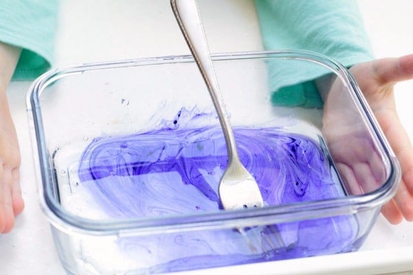Swirling purple slime in a clear container held by kid hands. In progress shot for slime with baking soda recipe.