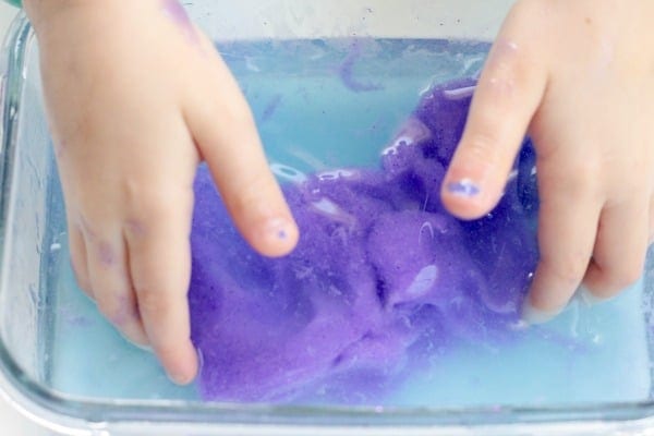 Child hands mixing a purple slime recipe with baking soda.