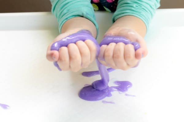 Making slime with baking soda holding purple slime in child hands.