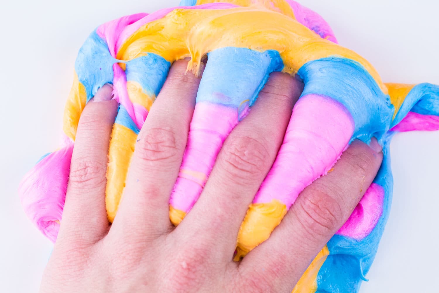 Hands covered in fluffy orange, blue, and pink slime showing the best fluffy slime recipe for the best slime ever.