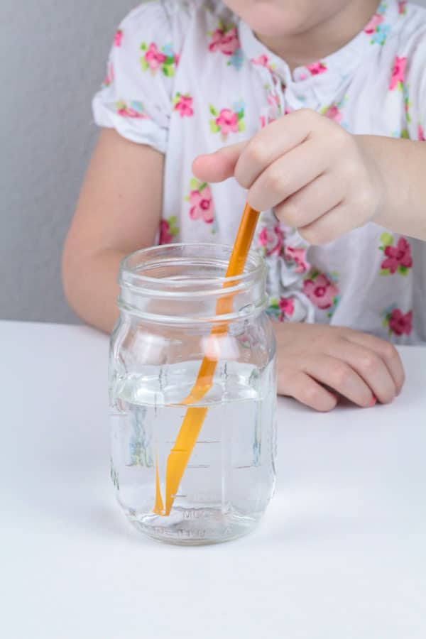 girl putting a pencil in a jar for the pencil in water experiment. 