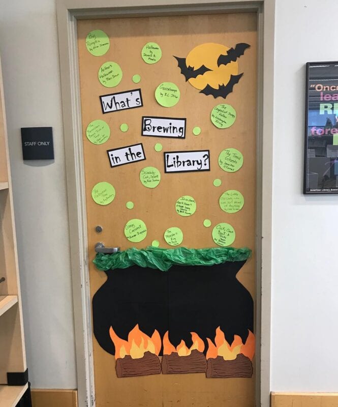 A classroom door decorated for halloween with a cauldron that says "What's brewing in the library?"